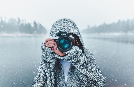 selective focus photo of a person holding black Nikon DSLR camera about to take a picture during snow season