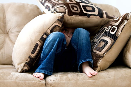 person wearing blue jeans hiding under throw pillows