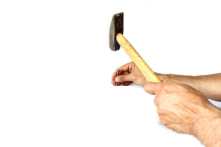 person's hand holding common nail and hammer