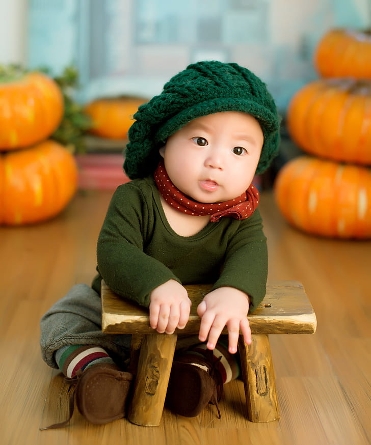 baby wearing green knitted cap, green crew-neck long-sleeved shirt and brown pants sitting near brown stool