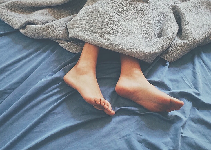 person laying on blue bed with gray blanket