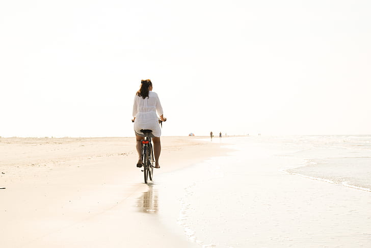 photo of woman riding bicycle near seashore