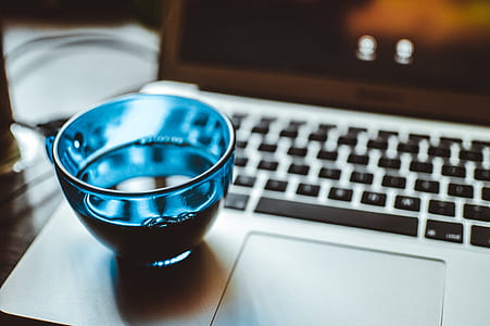 Shallow Focus Photography of Blue Glass Cup on Silver Laptop Computer