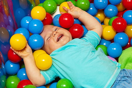 smiling toddler wearing blue t-shirt lying on assorted-color balls
