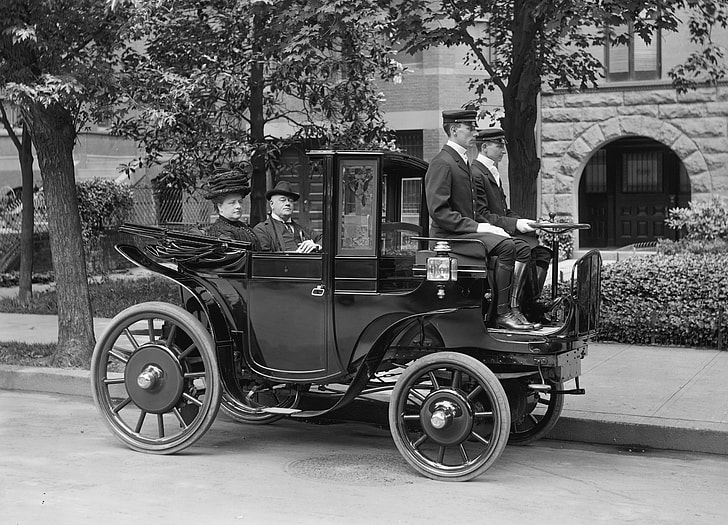 grayscale photograph of three men and one woman riding classic black vehicle