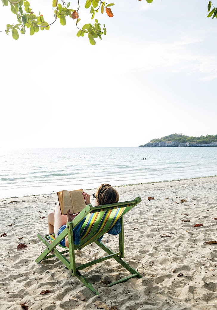photo of woman reading book near seashore