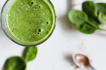 spinach juice on clear glass beside gray spoon