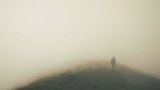man standing on high-ground surrounded by mist during daytime