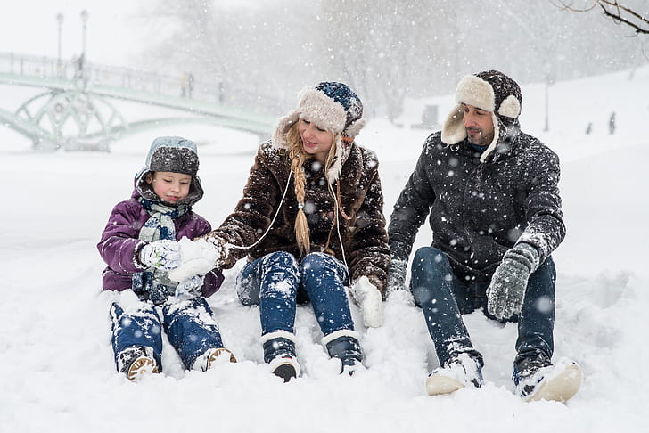 man, woman, and boy sitting on snow ground making snowballs