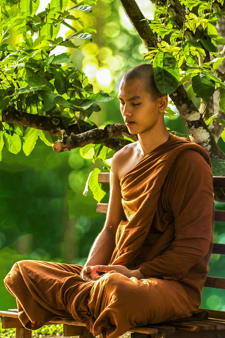 man wearing brown monk suit while sitting on bench near tree