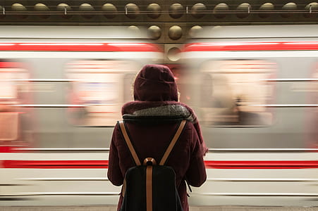 person wearing red hoodie carrying black leather backpack standing near train