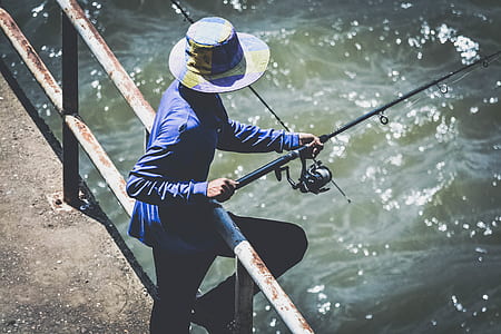 Person in Blue Long Sleeve Shirt and Black Pants Using Fishing Rod