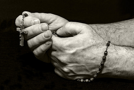 grayscale photo of human hands holding rosary