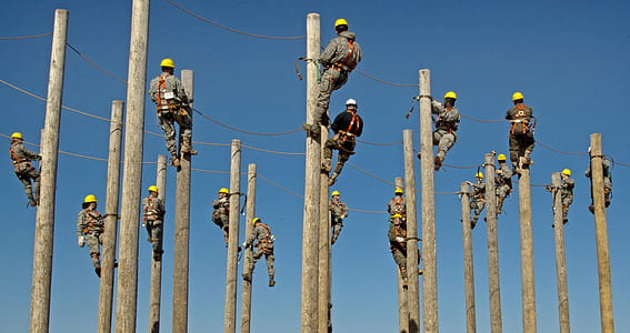 group of men wearing gray and black coveralls climbing electrical post during daytime