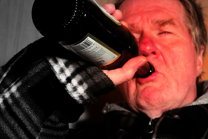 man wearing black zip-up jacket drinking on black and white labeled glass bottle