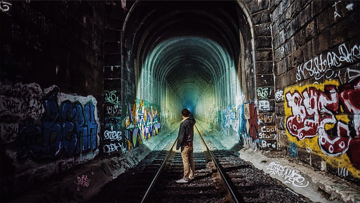 man standing in middle of train track tunnel