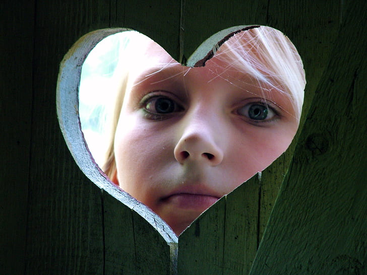 closeup photo of girl peeping on heart hole