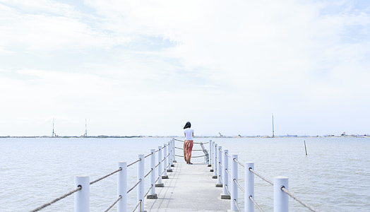 woman stands on sea dock under white clouds and blue sky