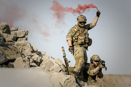 soldier holding a rifle while another soldier holding a colored smoke at the open field