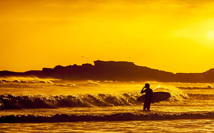 man holding surfboard during sunset