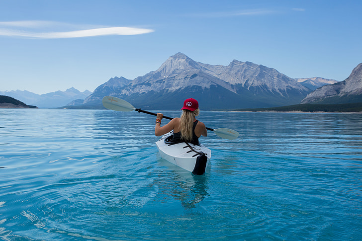 woman kayaking in calm body of water with mountain alps in distance during daytime