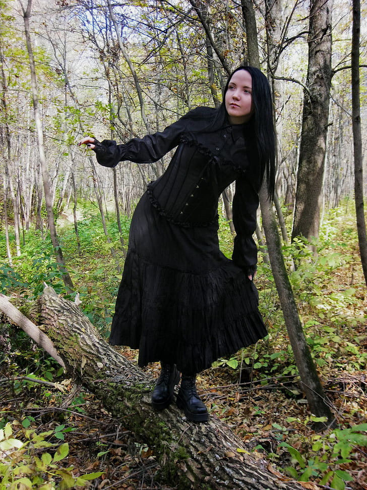 woman wearing black dress standing on brown tree log