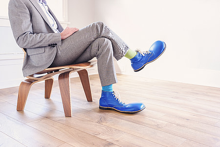 person sitting, wearing gray formal suit with pair of blue leather shoes