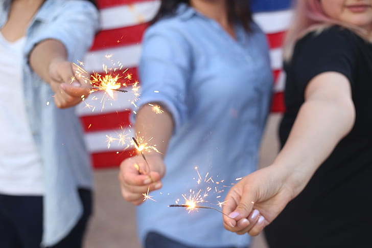 three person holds lighted sparkler firecrackers