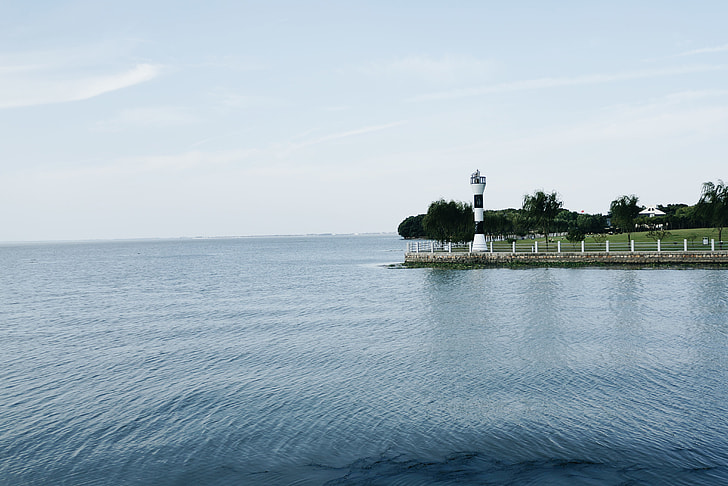 body of water near green island and lighthouse at daytime