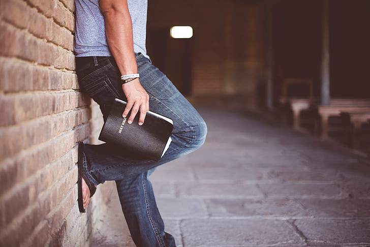 man holding book leaning on bricks