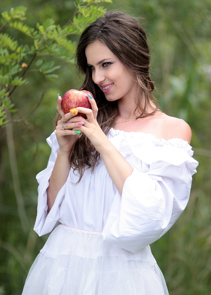 woman wearing white strapless elbow-sleeved dress holding honeycrisp apple