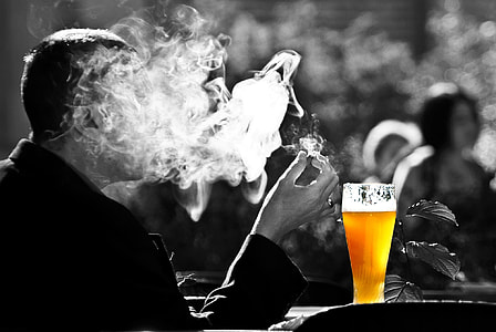 smoking man beside cup of beer selective color photography