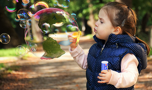 girl wearing blue and white polka-dot vest blowing bubbles during daytijme