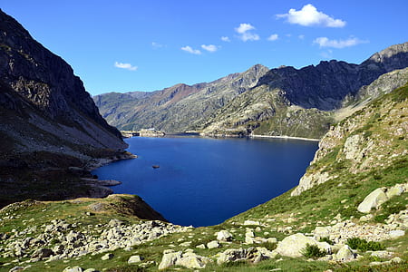 Mountain With Green Grass Beside Body of Water Under Blue Sky during Daytime