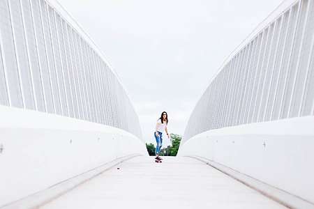 woman in white top and blue destressed jeans riding longboard beside white walls during daytime