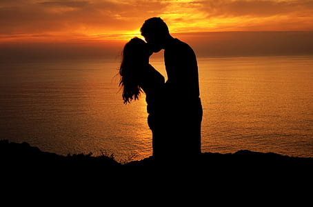 silhouette of man and woman kissing on cliff near body of water during golden hour