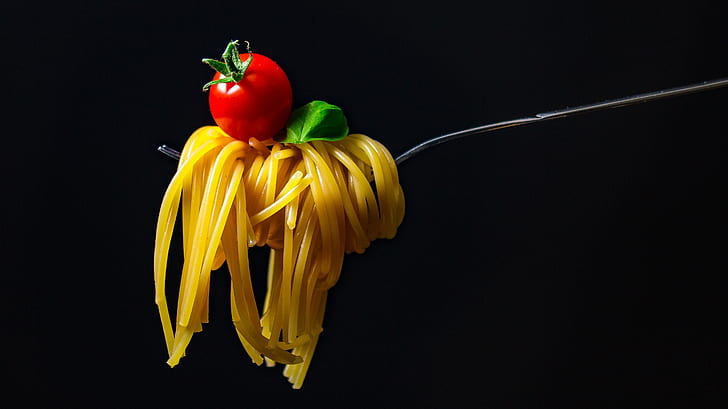rolled pasta in gray metal fork with red cherry tomato