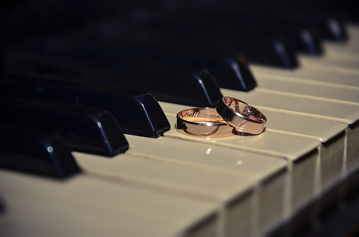 two pink gold-colored rings placed on piano keys