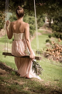 woman wearing pink strapless dress sitting on brown sing during daytime