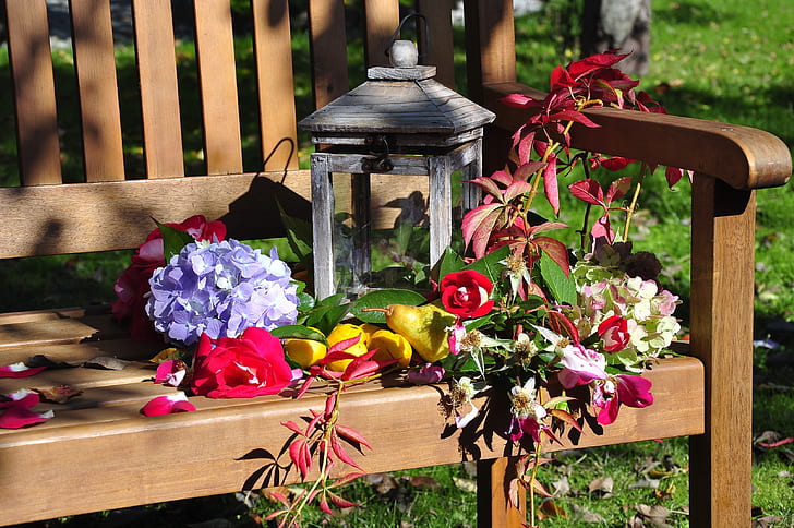 closeup photography of gray candle lantern on bench surrounded with flowers
