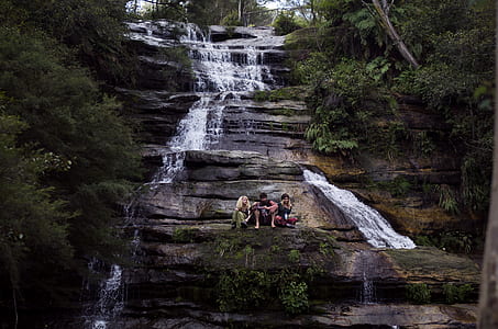 three person on cliff of waterfalls