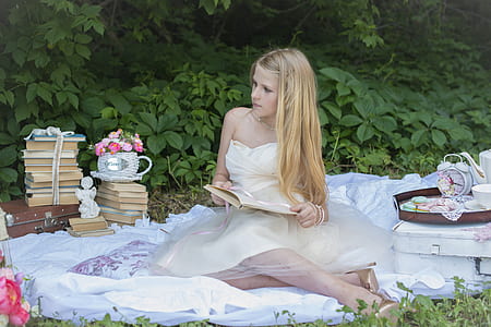 woman in white dress holding notebook while sitting on white textile during daytime