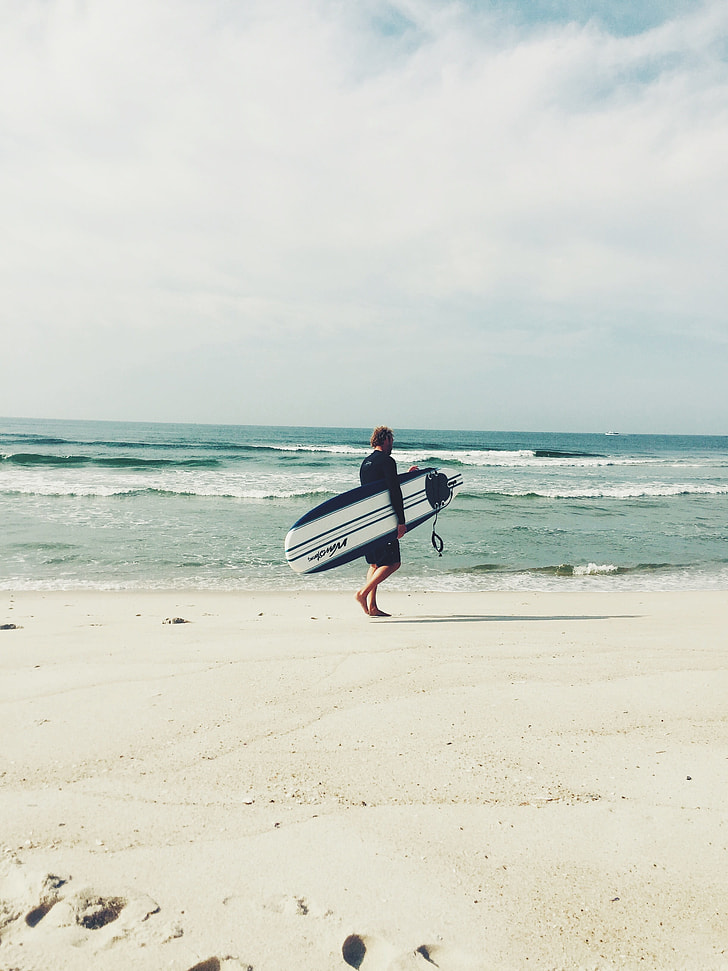man carrying white and blue surfboard walking on the seashore