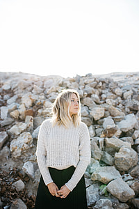 woman wearing gray knitted sweater and black skirt in front of rocks during daytime