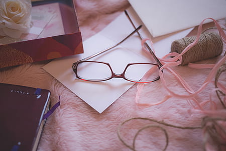 Eyeglasses Beside Pink Yarn on Pink Bed Blanket
