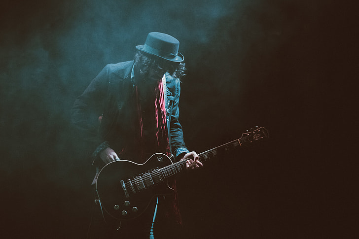 person wearing suit jacket and fedora hat playing guitar