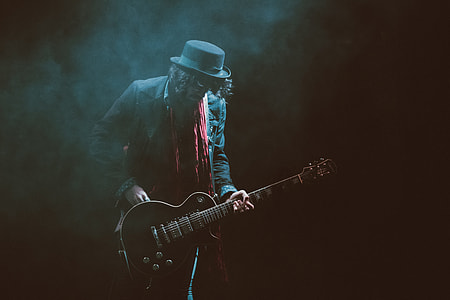 person wearing suit jacket and fedora hat playing guitar