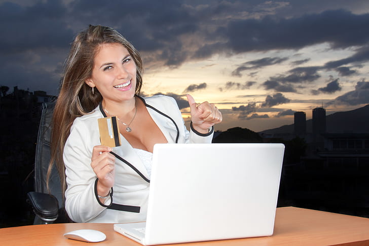woman wearing white blazer using MacBook White with credit card on her right hand outdoors