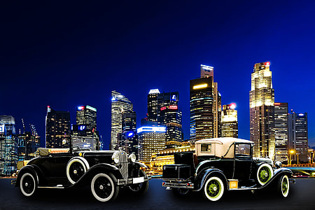 two vintage coupes near high-rise buildings taken during night time
