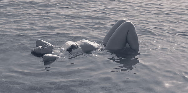 person in white bikini lying on body of water
